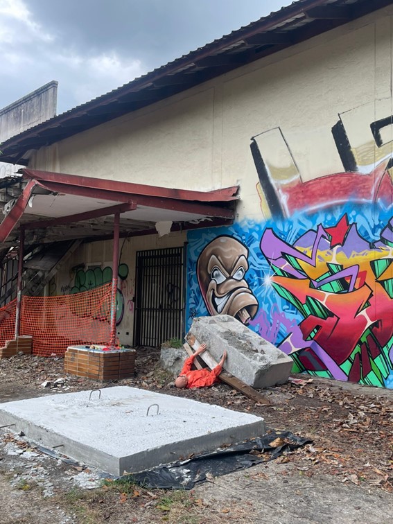 An industrial setting with grafitti on the walls shows a person (represented by a doll) trapped under rubble in the aftermath of an earthquake simulation.