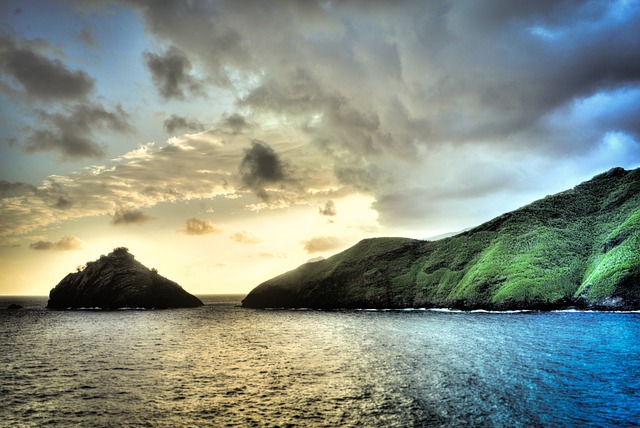 Sunset in the Pacific, showing dark clouds and golden light falling on water and a green island