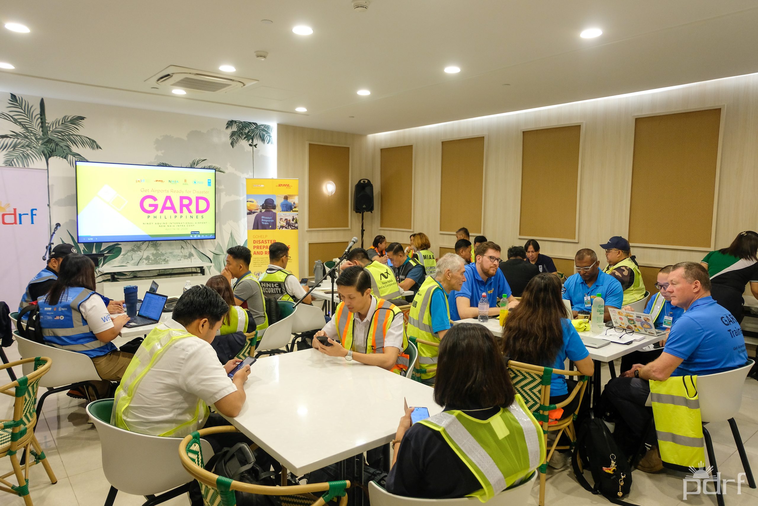 High-visibility vests instead of lanyards: staff from NNIC, DHL, the Manila International Airport Authority, the World Food Programme, and other agencies worked in small groups, table by table, mapping out capacity and constraints before taking the exercise outside onto the airfield itself. Photo credit: PDRF